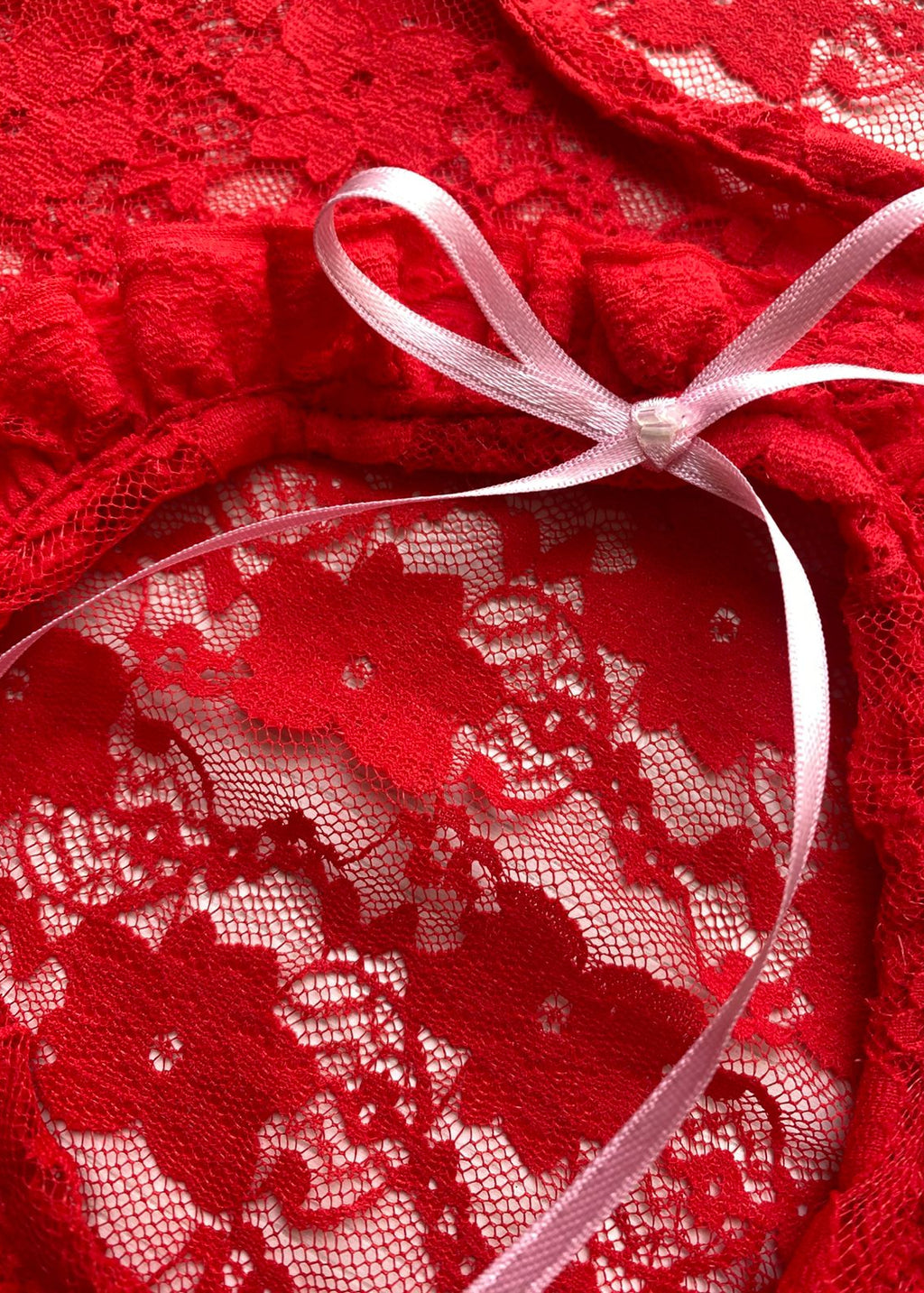 Top confeccionado en encaje suave y delicado, con una textura ligera que se adapta al cuerpo, creando un calce cómodo y favorecedor. Su diseño presenta una abertura frontal circular, enmarcada por un delicado fruncido, que aporta un detalle femenino y sutilmente sensual.

El lazo ajustable en el centro permite regular la abertura y añadir un toque romántico al diseño.