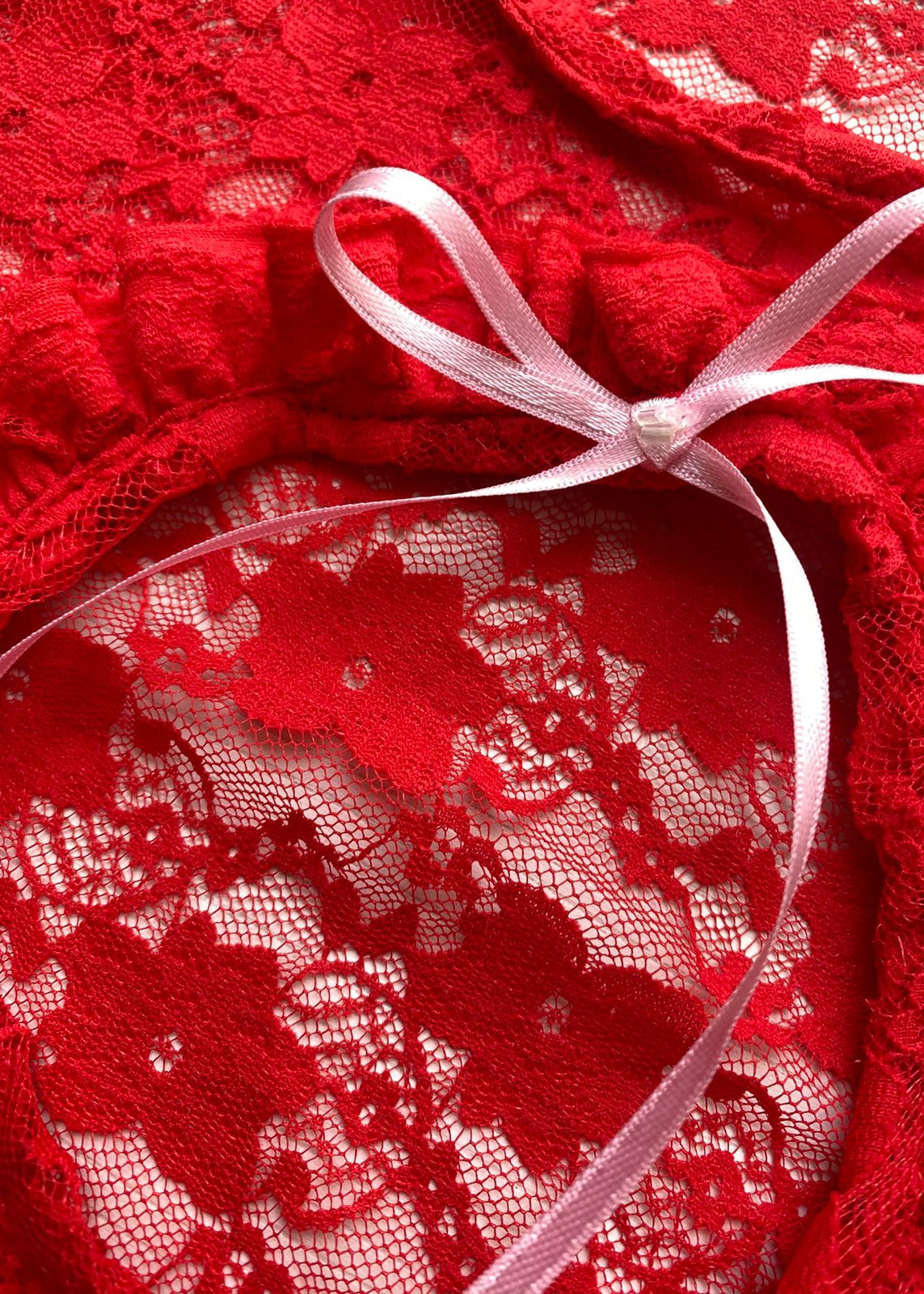 Top confeccionado en encaje suave y delicado, con una textura ligera que se adapta al cuerpo, creando un calce cómodo y favorecedor. Su diseño presenta una abertura frontal circular, enmarcada por un delicado fruncido, que aporta un detalle femenino y sutilmente sensual.

El lazo ajustable en el centro permite regular la abertura y añadir un toque romántico al diseño.