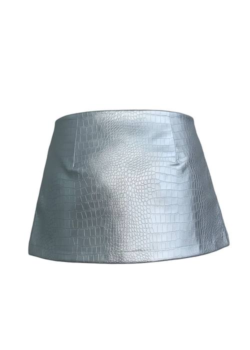 Mini falda confeccionada en cuerina con acabado metalizado, una tela que cede y se adapta al cuerpo, realzando la silueta sin perder estructura.

Cuenta con una correa de la misma cuerina, cosida directamente a la falda, que incorpora ojales metálicos, aportando un detalle moderno y funcional. Su silueta recta y corta le da un aire contemporáneo con una estética limpia y editorial.

