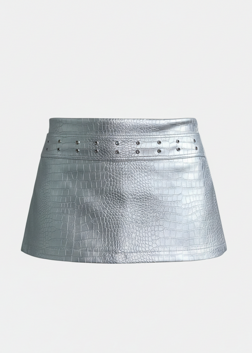Mini falda confeccionada en cuerina con acabado metalizado, una tela que cede y se adapta al cuerpo, realzando la silueta sin perder estructura.

Cuenta con una correa de la misma cuerina, cosida directamente a la falda, que incorpora ojales metálicos, aportando un detalle moderno y funcional. Su silueta recta y corta le da un aire contemporáneo con una estética limpia y editorial.

